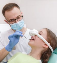 Professional dentist examining teeth of young girl, using inhalation sedation mask on her